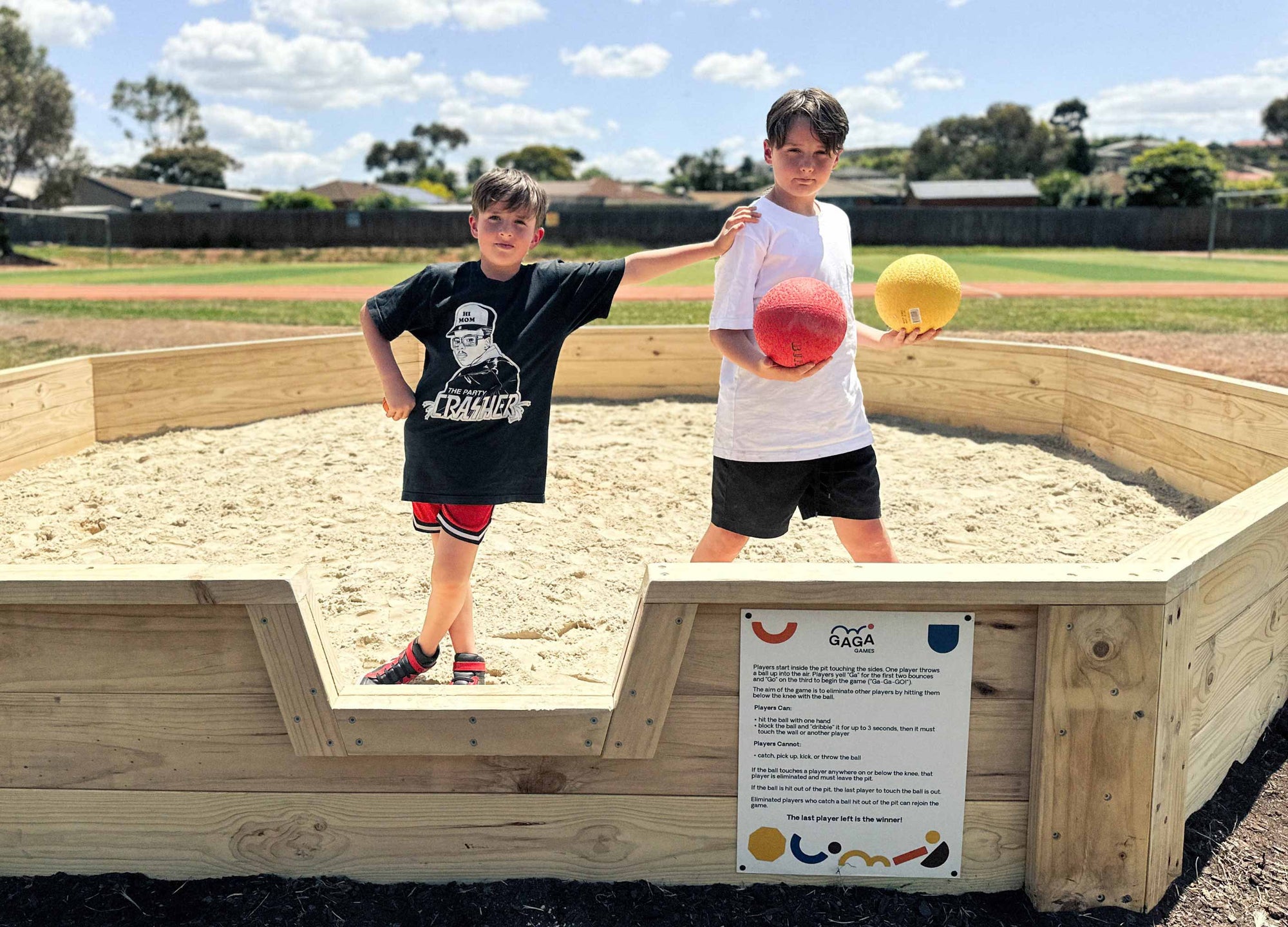 Two children standing seriously in a Gaga Ball Pit, one is holding a Gaga ball, ready to play, posing for the camera.