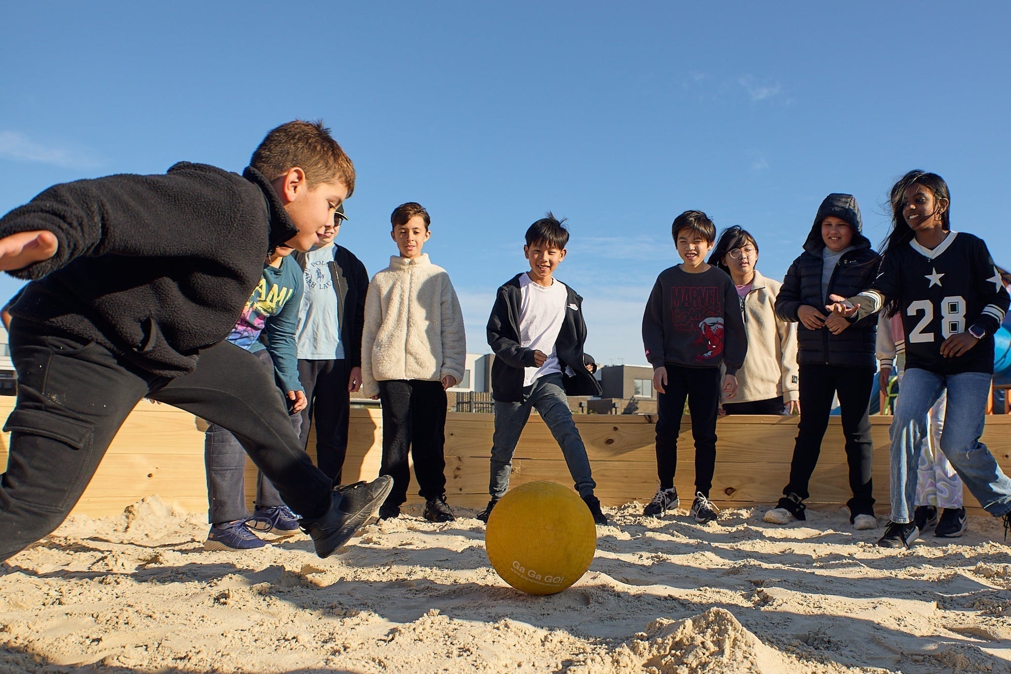 Kids playing gaga ball in an outdoor gaga pit with a yellow ball